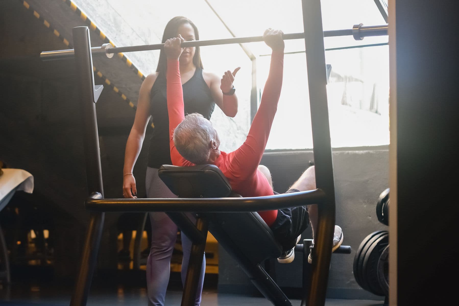 Trainerin begleitet einen älteren Mann beim Krafttraining in heller, freundlicher Umgebung