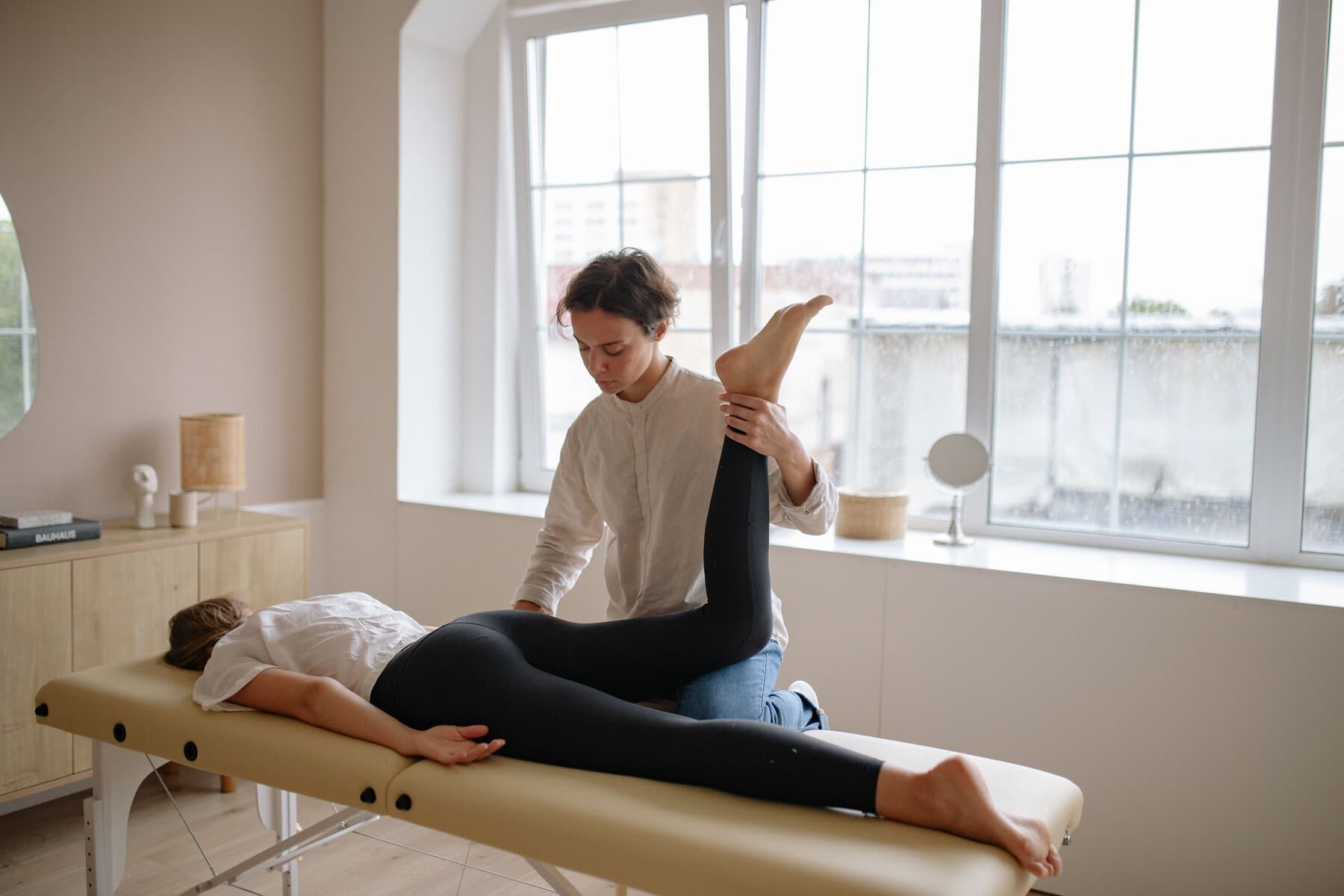 Physiotherapeutin dehnt entspannt das Bein einer Patientin in einem hellen Behandlungsraum